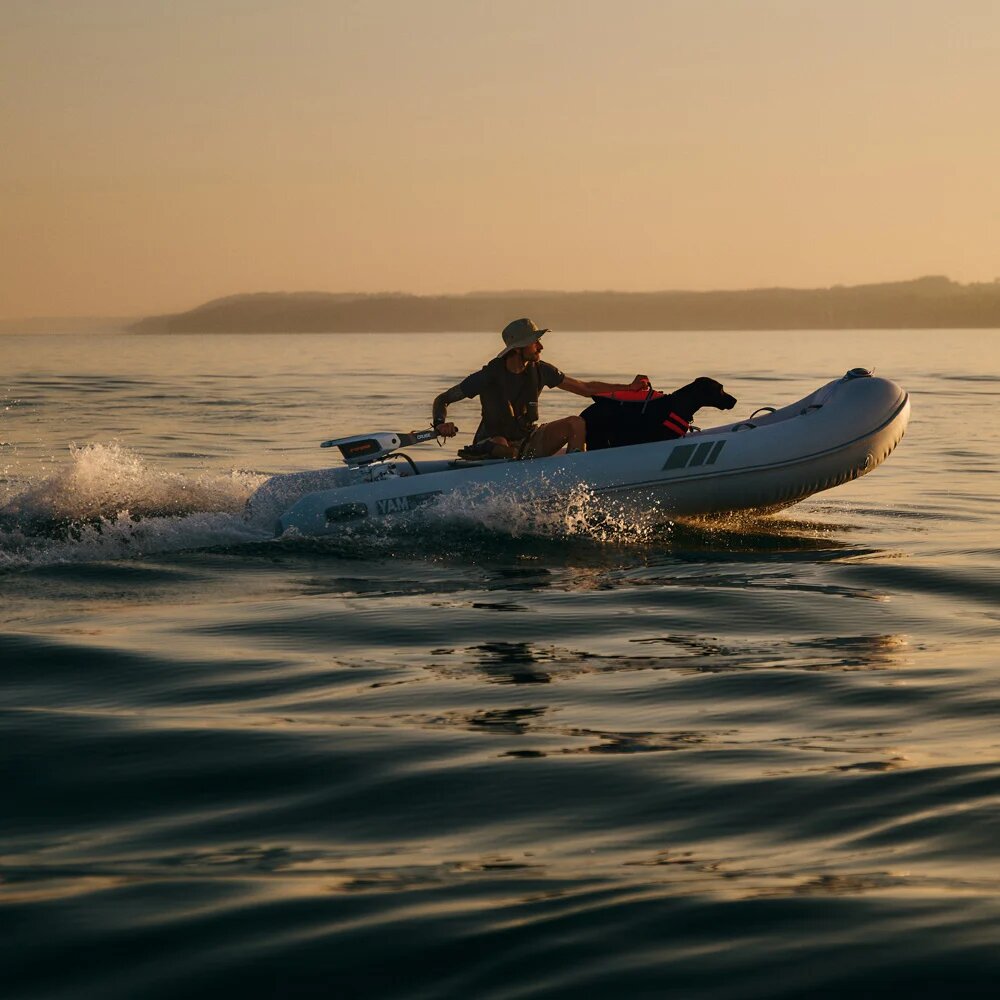 Electric outboard driving a rigid inflatable across calm water at sunset