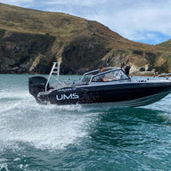 A UMS 655 DC aluminum boat speeding across coastal waters near rugged cliffs.