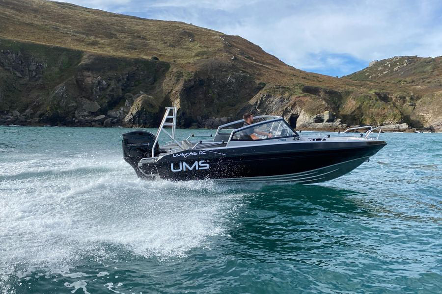 A UMS 655 DC aluminum boat speeding across coastal waters near rugged cliffs.