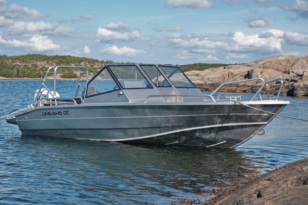 An aluminum UMS 545 DC boat anchored near a rocky shore.