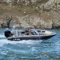 A man steering the UMS 655 DC aluminum boat at speed near a rocky shoreline.