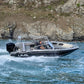 A man driving the UMS 655 DC aluminum boat at high speed near a rocky shoreline.