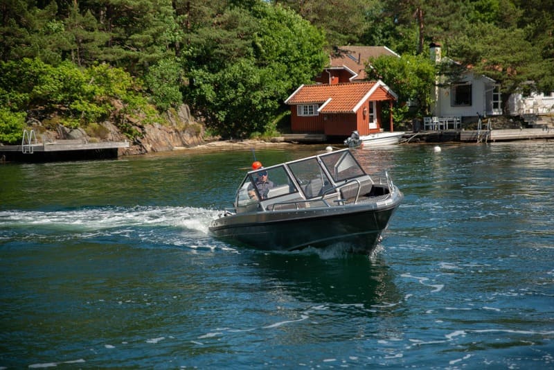 A UMS 585DC boat navigating a serene, wooded lakeside area.