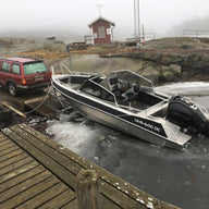 A UMS 600 DC aluminum boat being launched into icy waters from a trailer hitched to a red SUV.