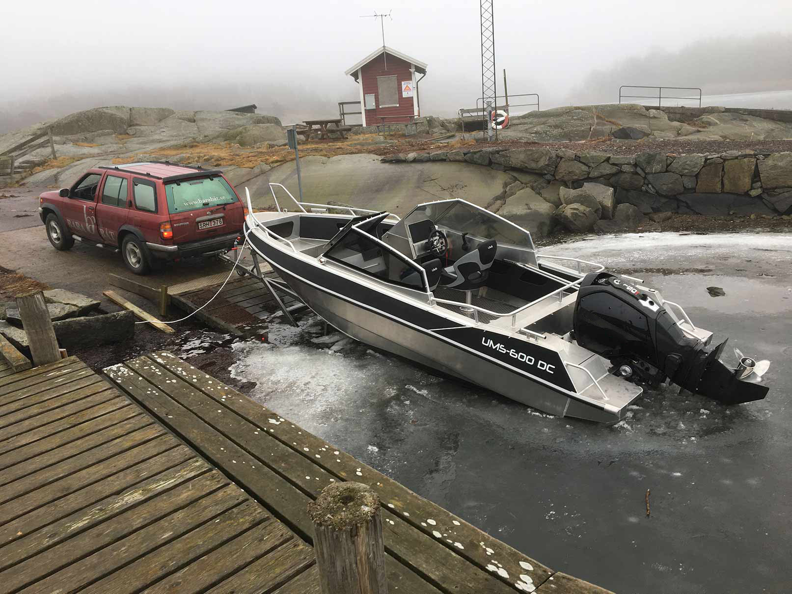 A UMS 600 DC aluminum boat being launched into icy waters from a trailer hitched to a red SUV.