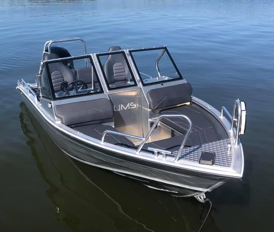 A sleek Aluminum Boat UMS 485 DC is shown docked on calm water, highlighting its modern design and spacious interior with dual consoles.
