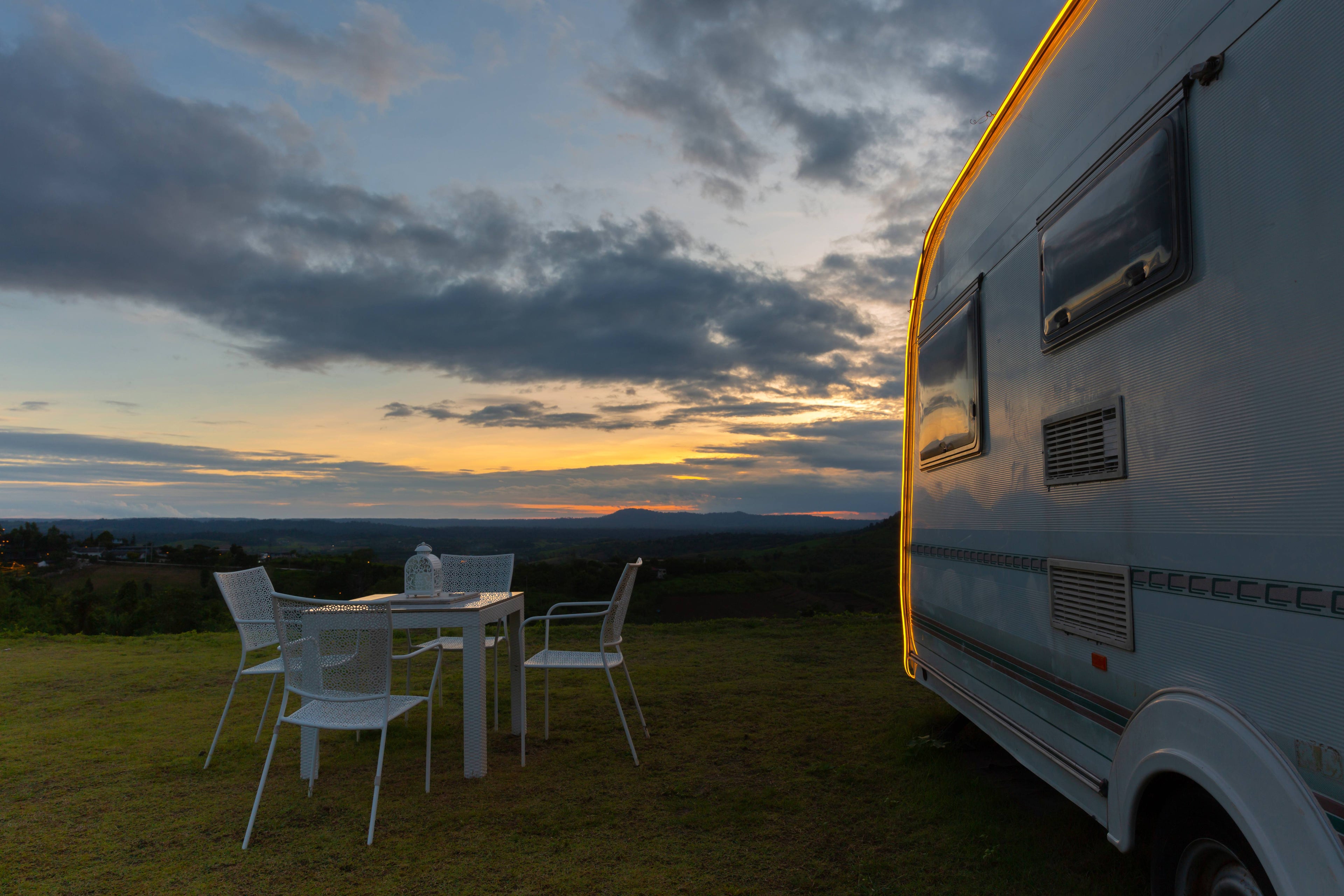 RV parked outdoors with a sunset view and table with chairs.