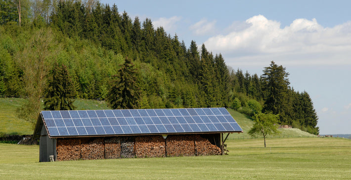 Barn with solar panels on the roof in a rural setting with trees and grass.