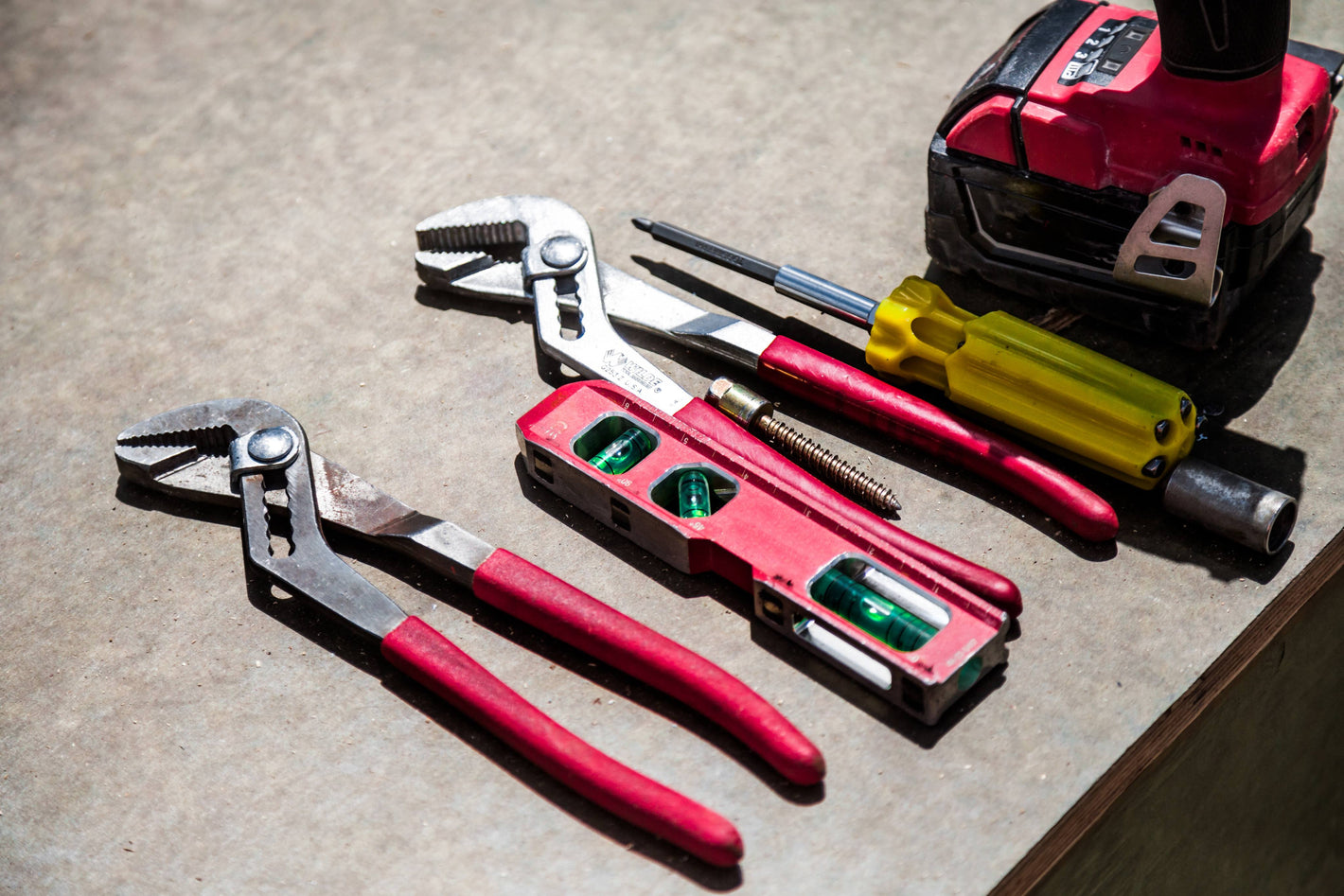 Pliers, spirit level, screwdriver, and cordless drill laid out on a workbench