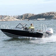 A person is driving an Aluminum Boat UMS 485 DC on open water near rocky shores, showcasing the boat's performance and design.